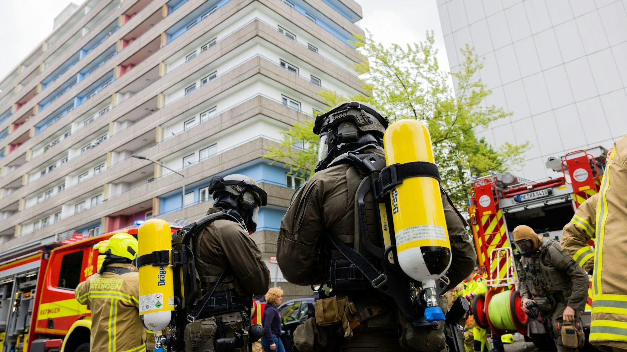 Polizeibeamte mit Gasmasken und Feuerwehrleute stehen während des Einsatzes vor dem Hochhaus in Ratingen.