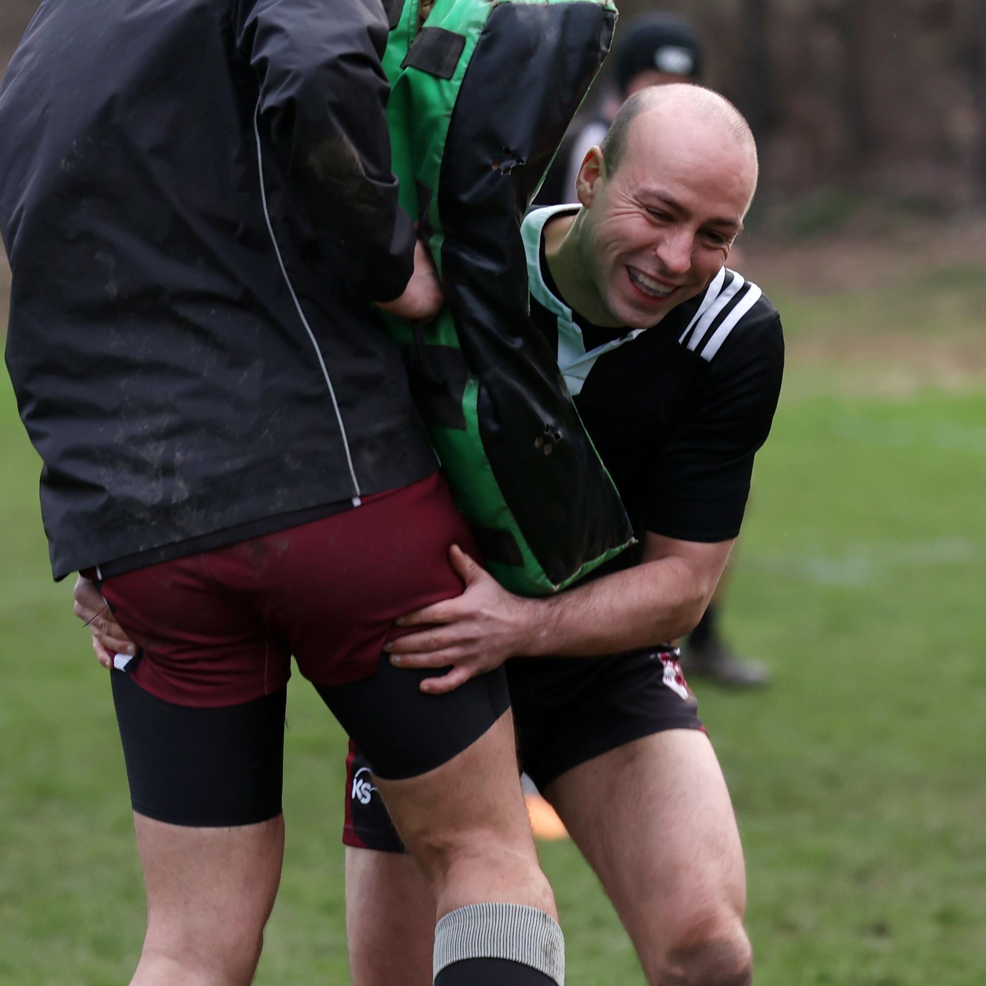 Ein junger Rugby-Spieler in Aktion, er stemmt sich gegen die Schutzmatte, die der Trainingsgegner vor seinen Körper hält.