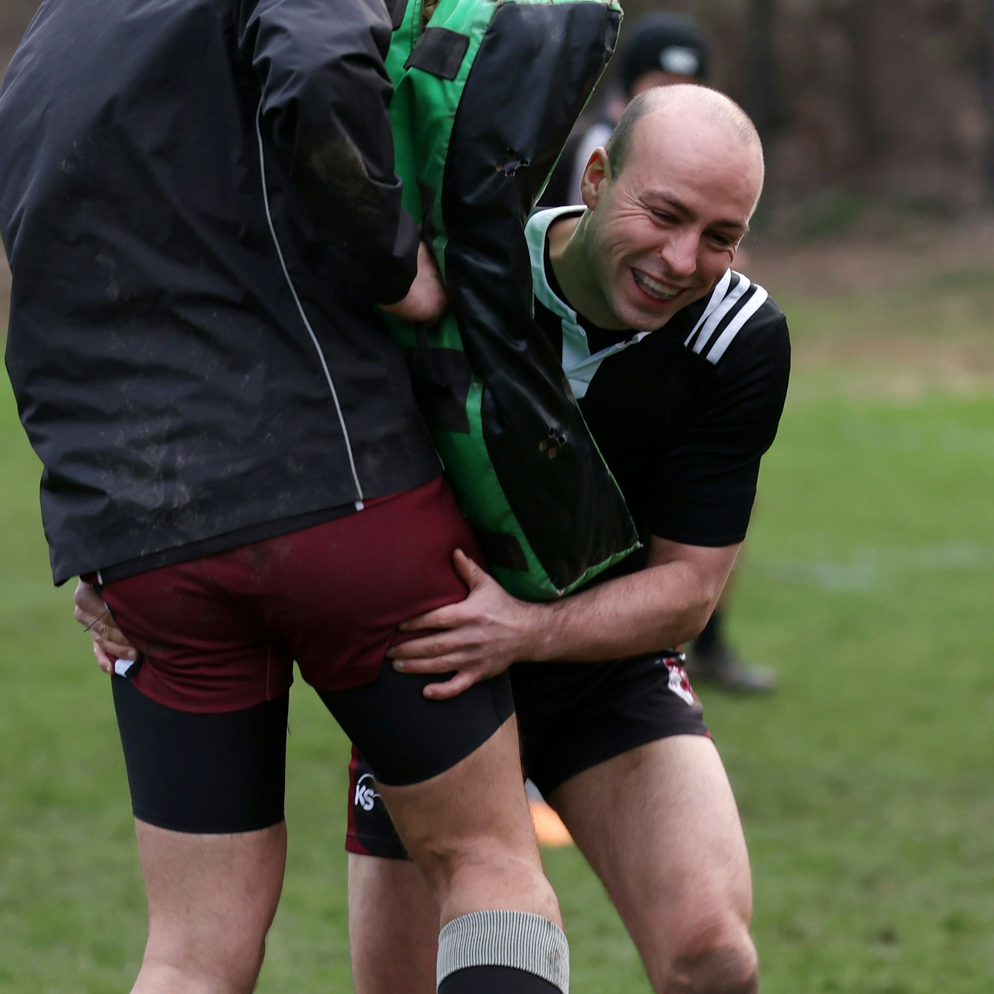 Ein junger Rugby-Spieler in Aktion, er stemmt sich gegen die Schutzmatte, die der Trainingsgegner vor seinen Körper hält.