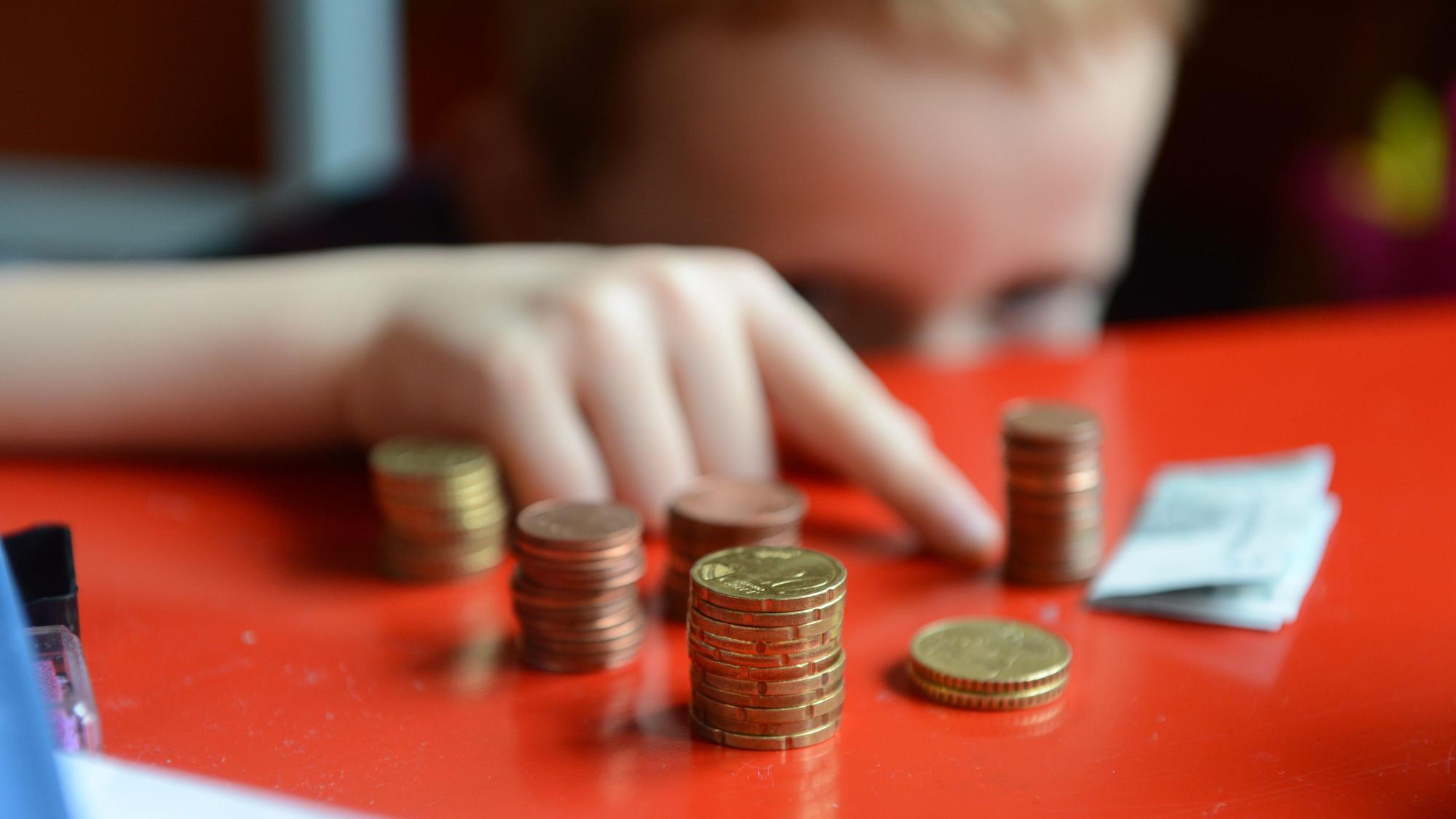Ein fünfjähriger Junge sitzt an einem roten Tisch und zählt sein gespartes Taschengeld.