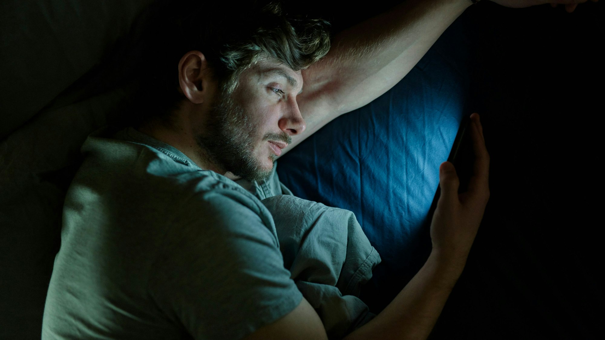 Ein Mann liest im Bett auf dem Smartphone