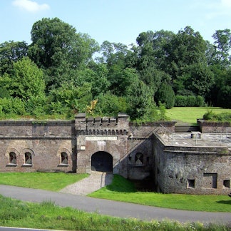Zu sehen ist ein festungsähnlicher Bau mit viel Grün drumherum.