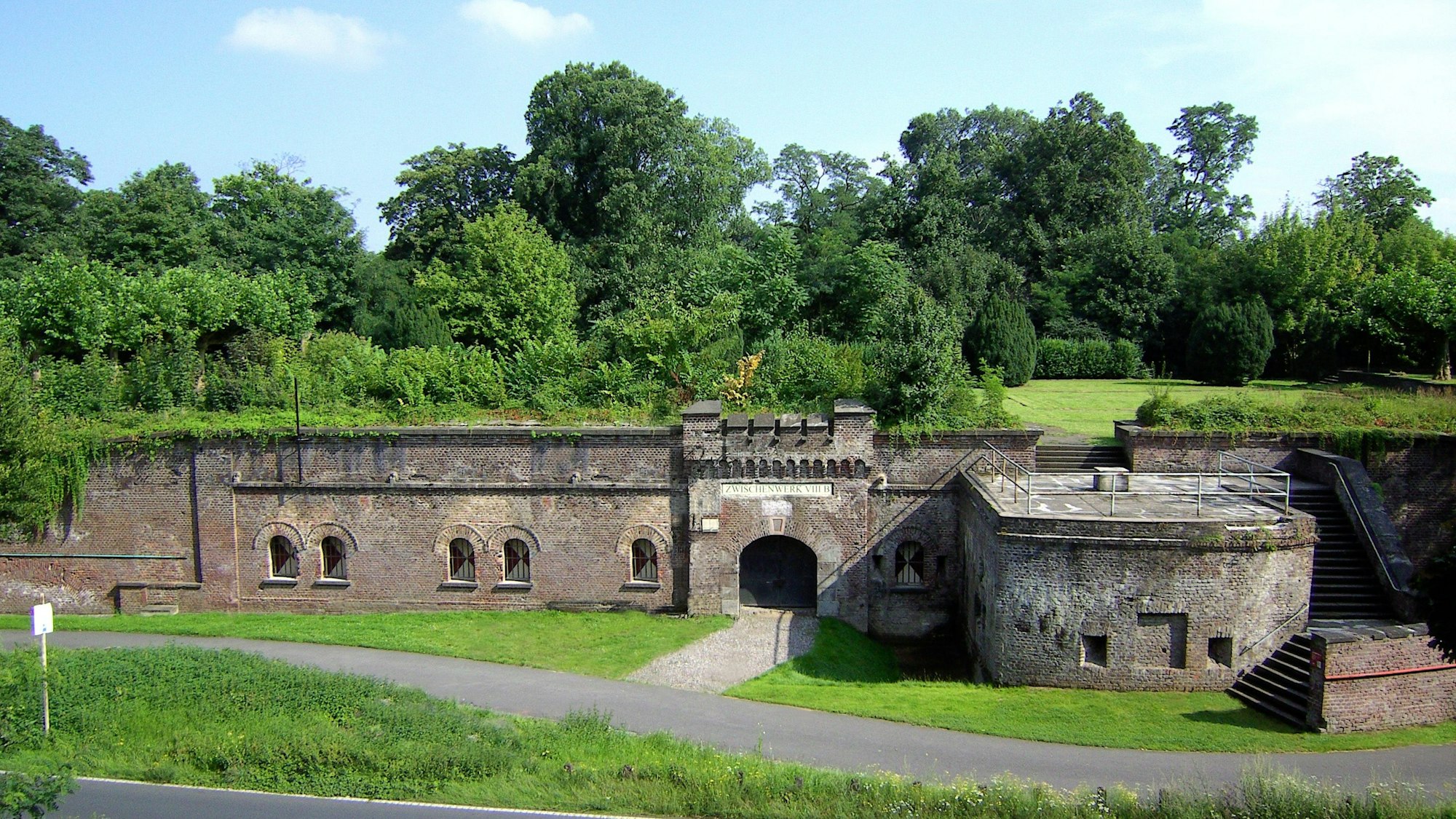 Zu sehen ist ein festungsähnlicher Bau mit viel Grün drumherum.