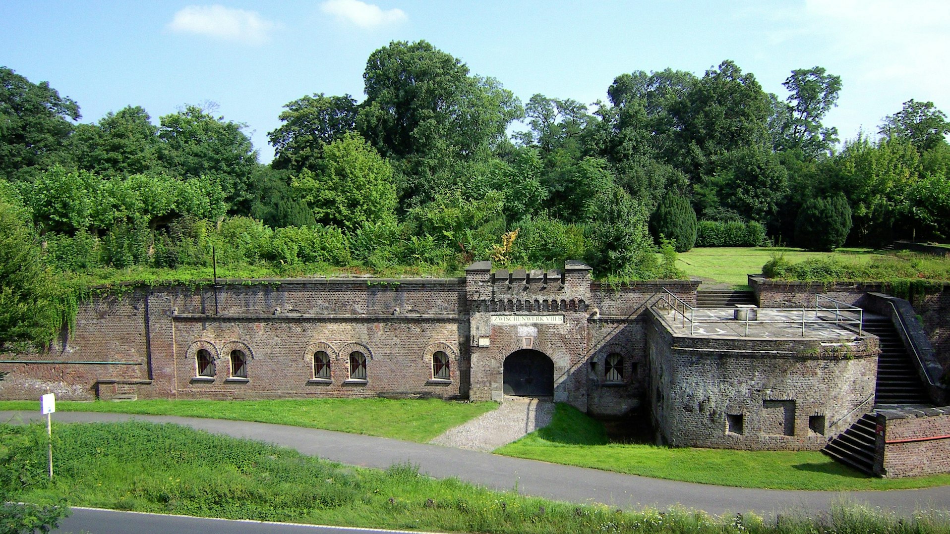 Zu sehen ist ein festungsähnlicher Bau mit viel Grün drumherum.