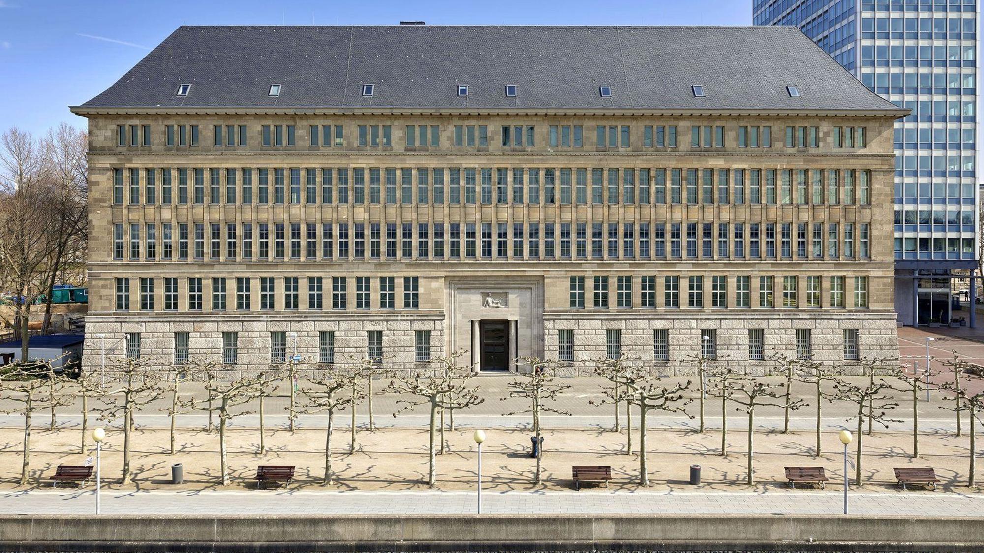 Die Fassade des Behrensbaus am Düsseldorfer Rheinufer ist zu sehen, davor Platanen, noch ohne Blätter.