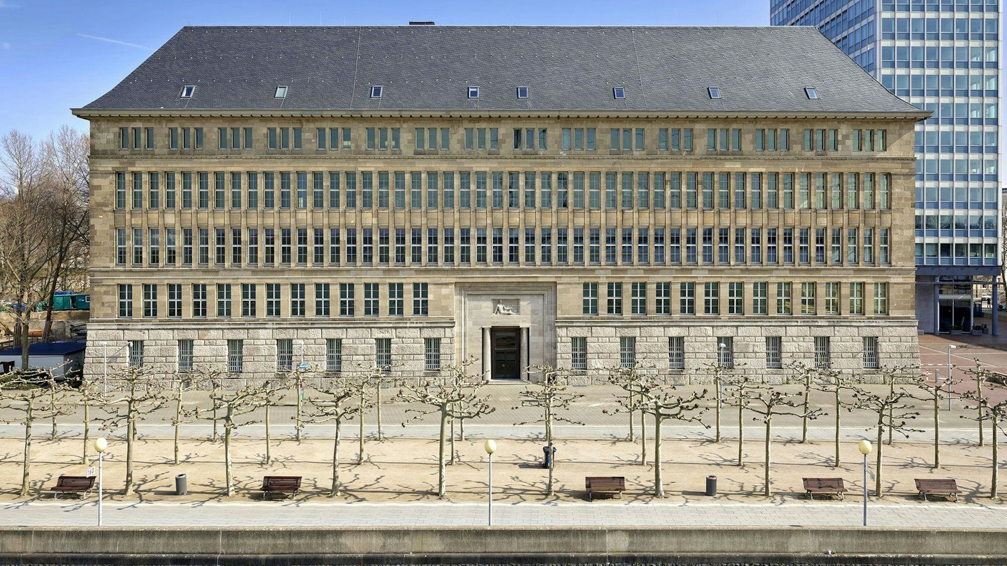 Die Fassade des Behrensbaus am Düsseldorfer Rheinufer ist zu sehen, davor Platanen, noch ohne Blätter.