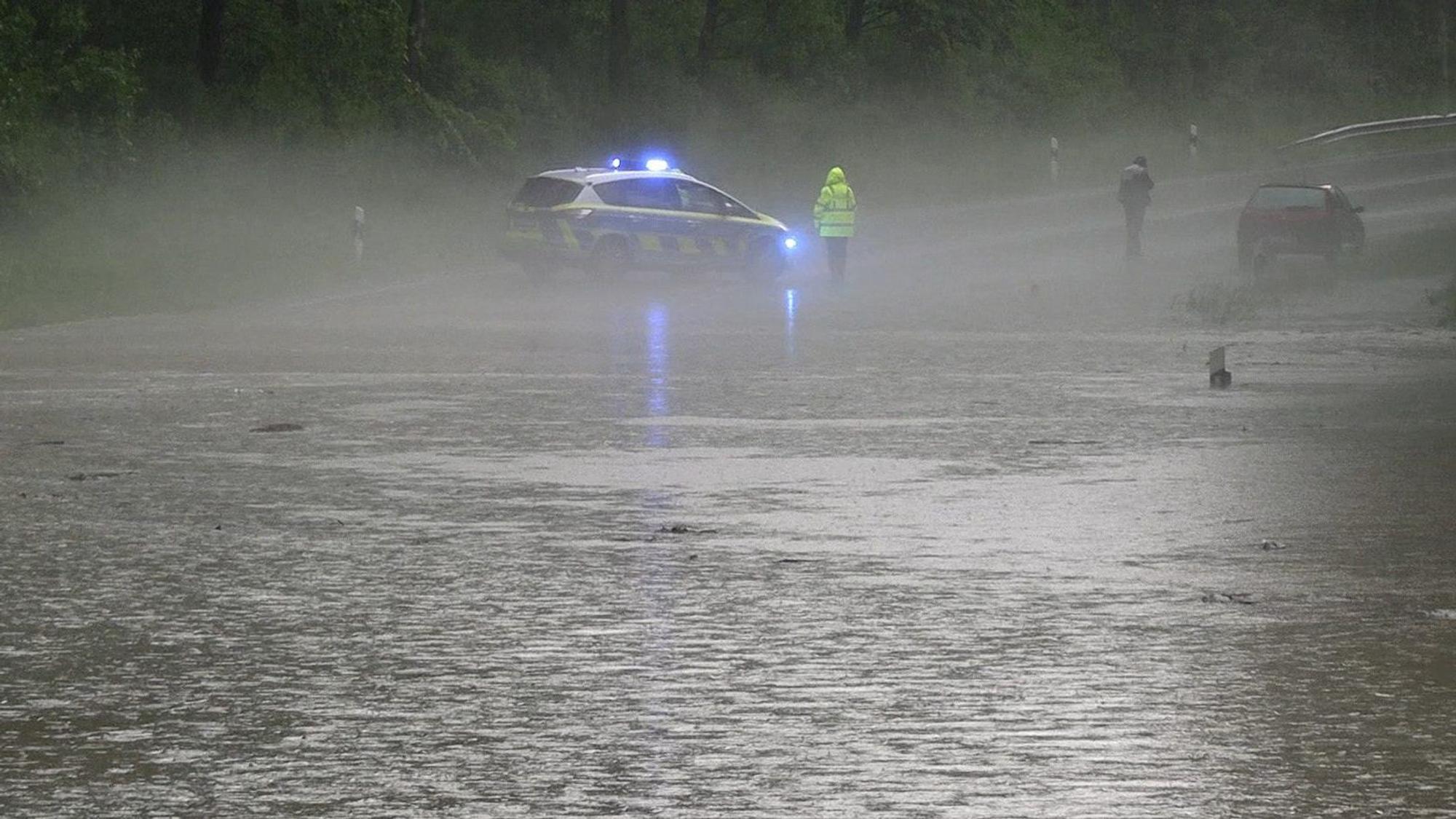 Schwere Unwetter in Detmold (Ostwestfalen-Lippe): Ein Polizist und ein Autofahrer stehen an einer überfluteten Straße nach dem Starkregen am Montagabend.
