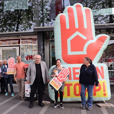 Menschen mit Plakaten stehen vor einem Flachbau.