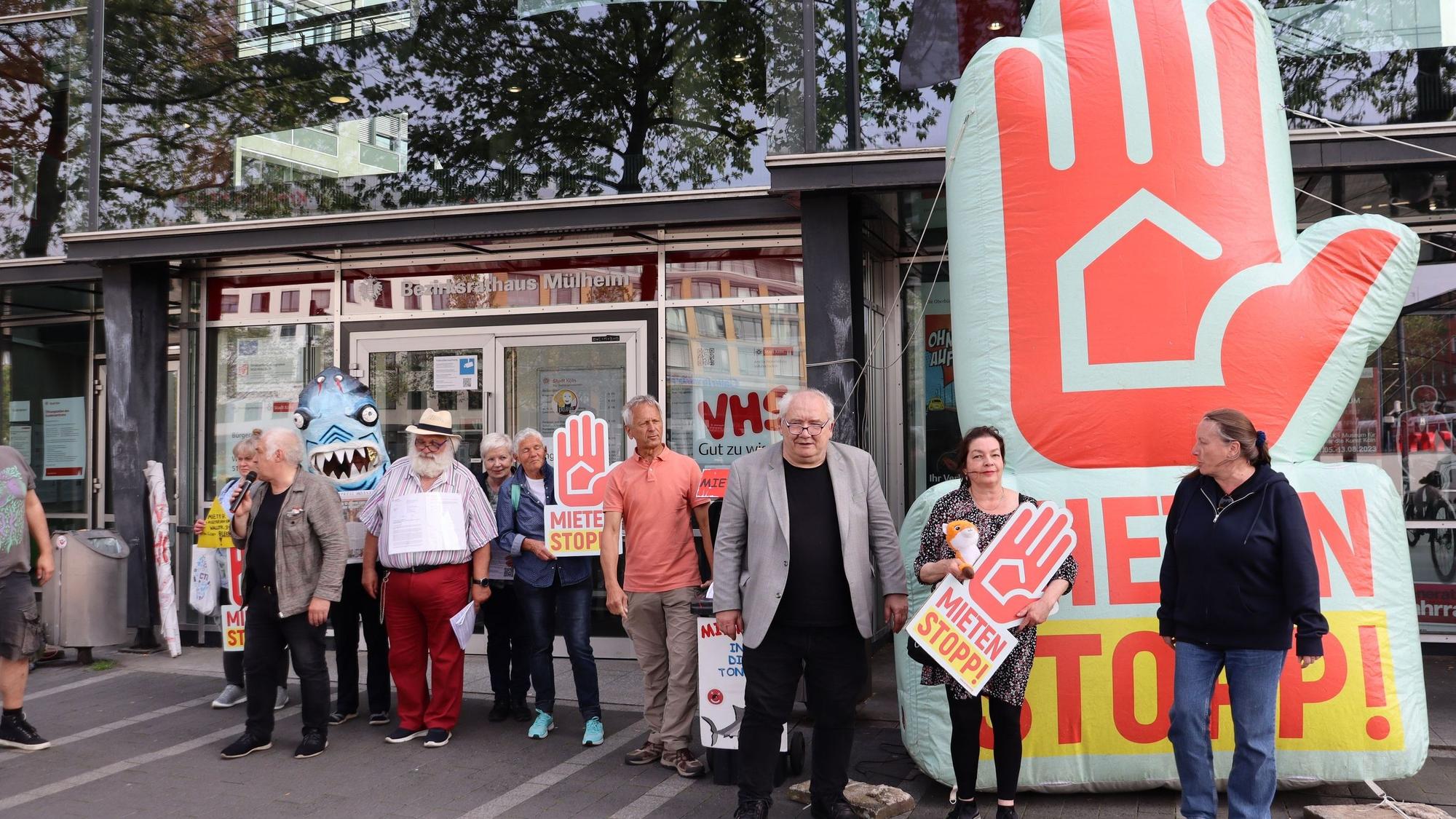 Menschen mit Plakaten stehen vor einem Flachbau.