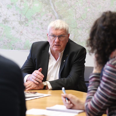 Ein Mann im Anzug ist im Gespräch mit zwei Redakteuren.