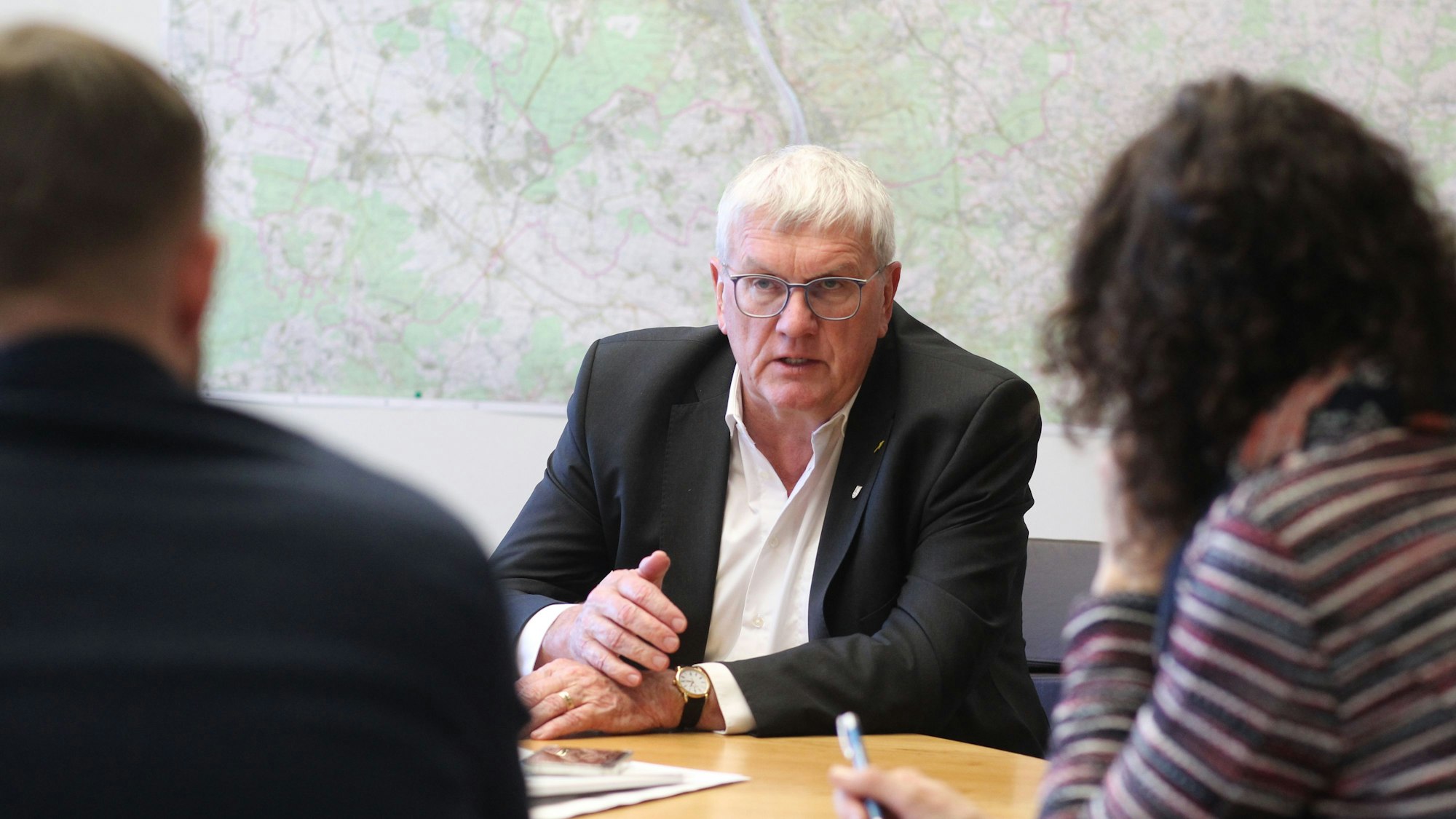 Ein Mann im Anzug ist im Gespräch mit zwei Redakteuren.