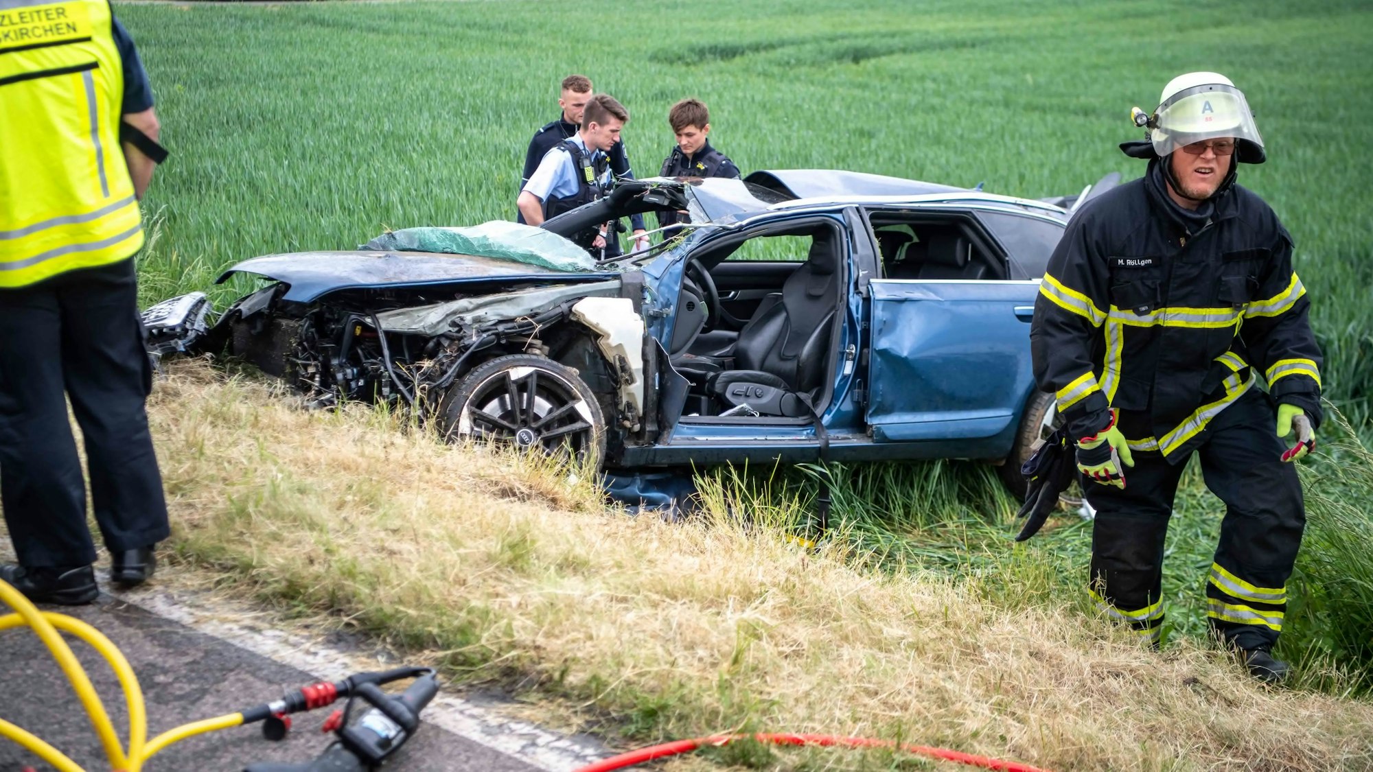 Drei Polizisten begutachten den zerstörten Audi. Auch die Feuerwehr war nach Unfall bei Kleinbüllesheim im Einsatz.