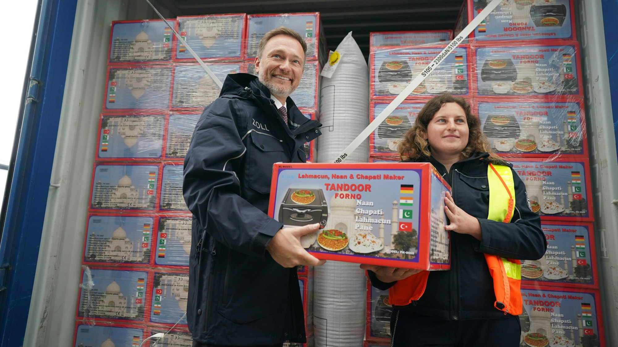 Christian Lindner (FDP, l), Bundesminister der Finanzen, und Katharina Lorenzen, Zollinspektorin, tragen einen Karton mit einem elektrischen Tischofen von einem Lkw-Container zu einem mobilen Röntgengerät während Lindners Besuch in der Zollabfertigung im Zollamt Hamburg.