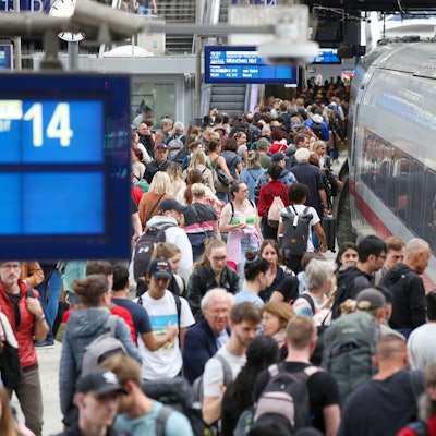 Zahlreiche Reisende sind auf einem vollen Bahnsteig unterwegs.