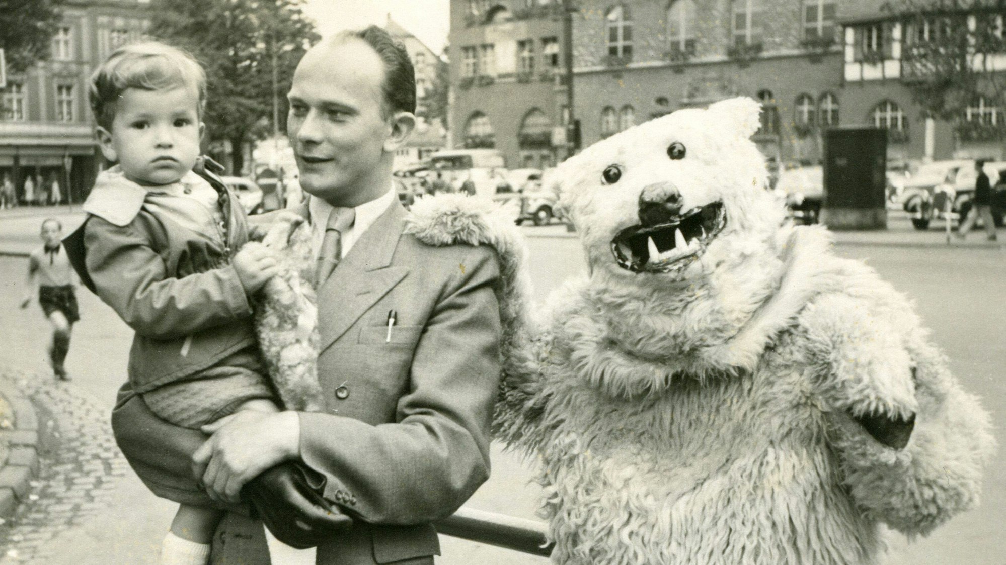 Es ist der kleine Unrau auf dem Arm seines Vaters, neben einem verkleideten Bären zu sehen.