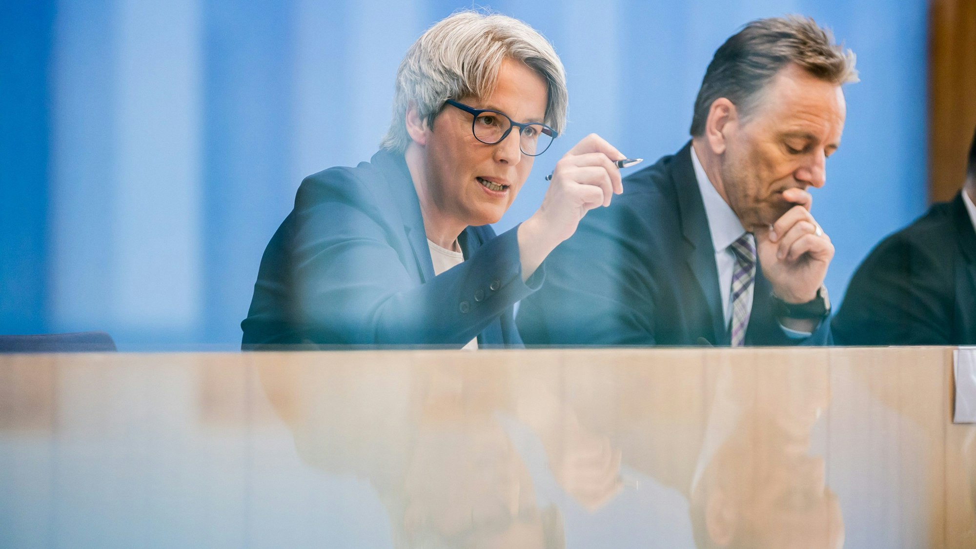 Eine Frau mit Brille und ein Mann werden auf einem Pult gespiegelt.