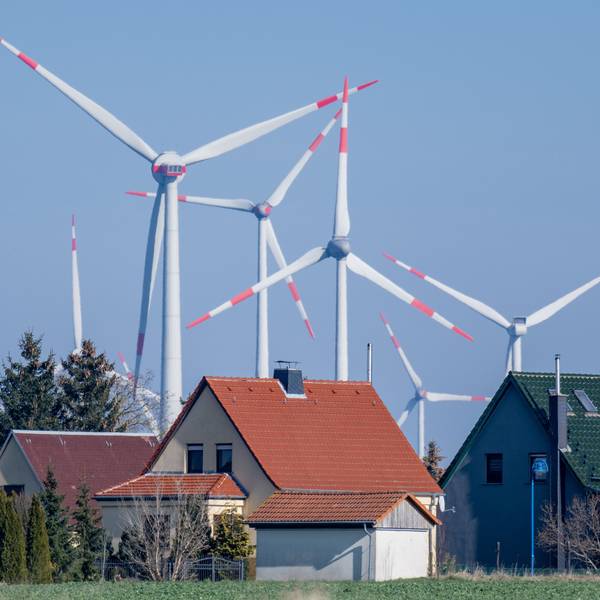 ARCHIV - 01.03.2023, Sachsen-Anhalt, Wethau: Windräder drehen sich hinter einer Siedlung mit Eigenheimen bei Wethau in Sachsen-Anhalt. Strom und Gas werden für einige Haushaltskunden etwas günstiger - allerdings oft auf hohem Niveau.