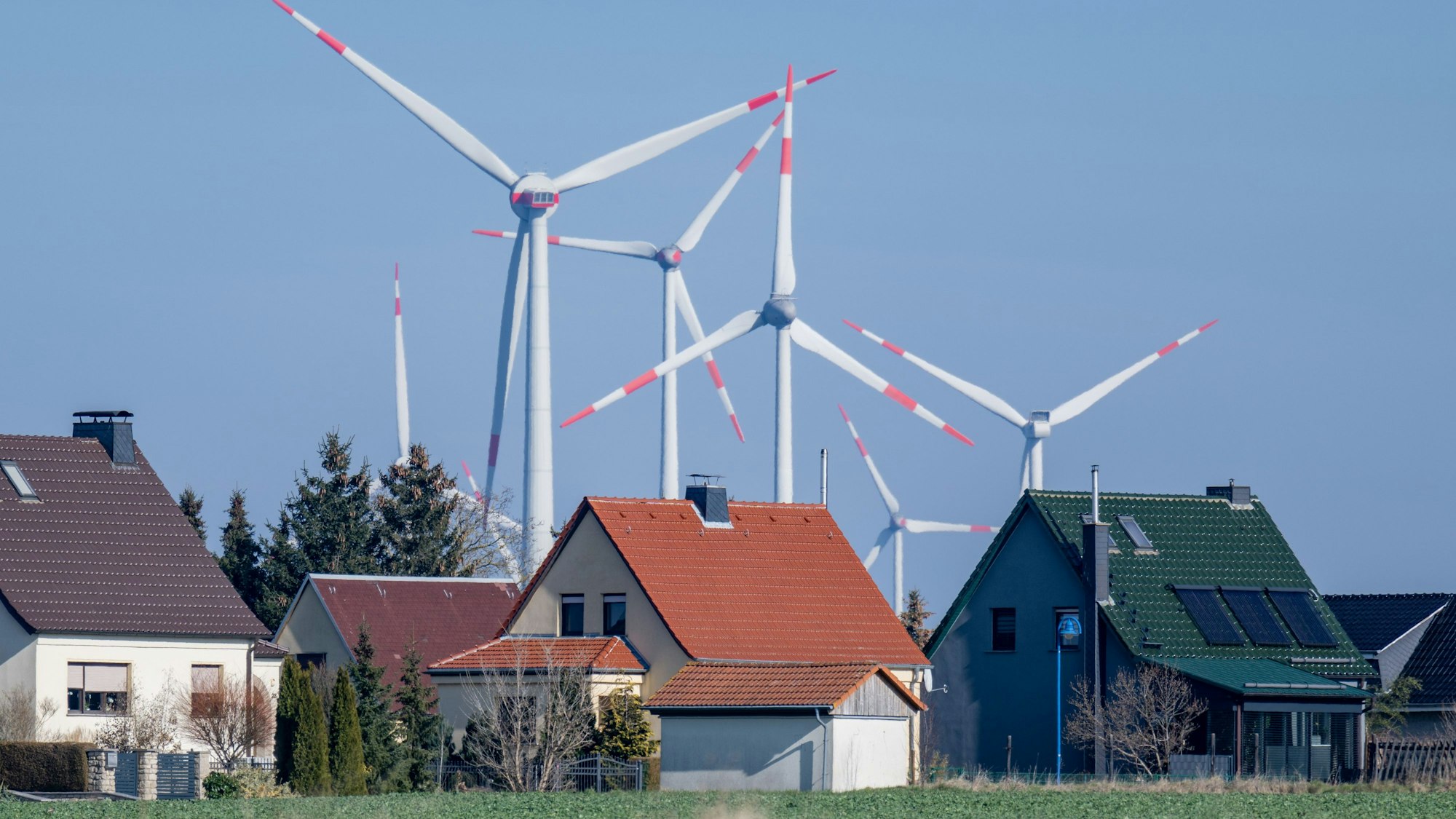 ARCHIV - 01.03.2023, Sachsen-Anhalt, Wethau: Windräder drehen sich hinter einer Siedlung mit Eigenheimen bei Wethau in Sachsen-Anhalt. Strom und Gas werden für einige Haushaltskunden etwas günstiger - allerdings oft auf hohem Niveau.