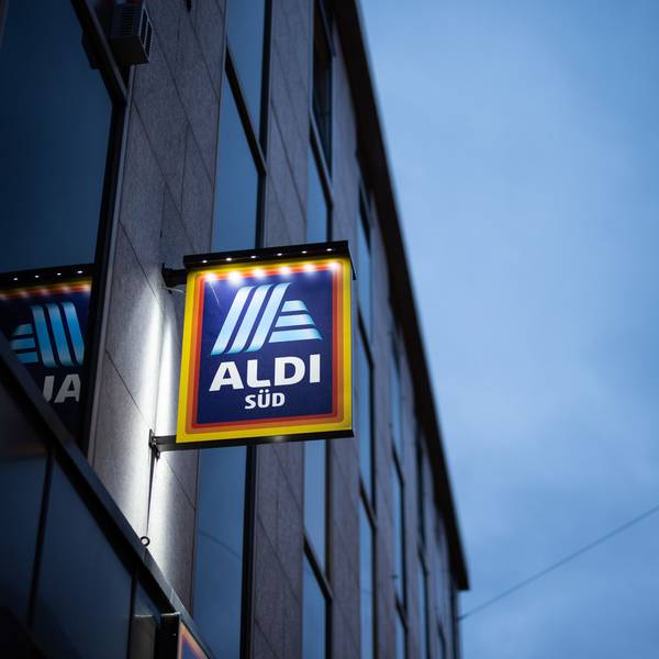 Das Logo einer Aldi Süd Filiale, fotografiert kurz vor dem Sonnenuntergang. Das Schild wird beleuchtet.
