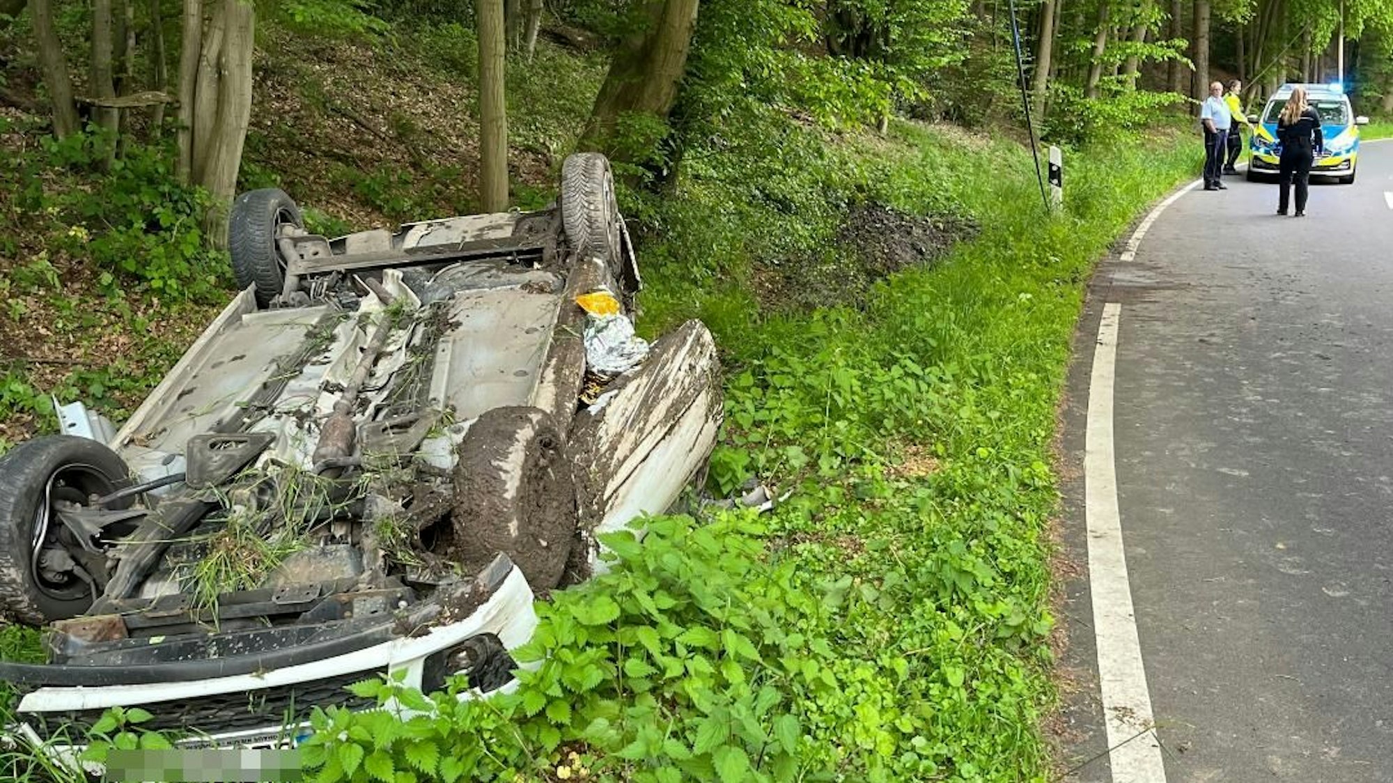 Das Auto liegt auf dem Dach im Straßengraben. Im Hintergrund ist die Polizei zu sehen.
