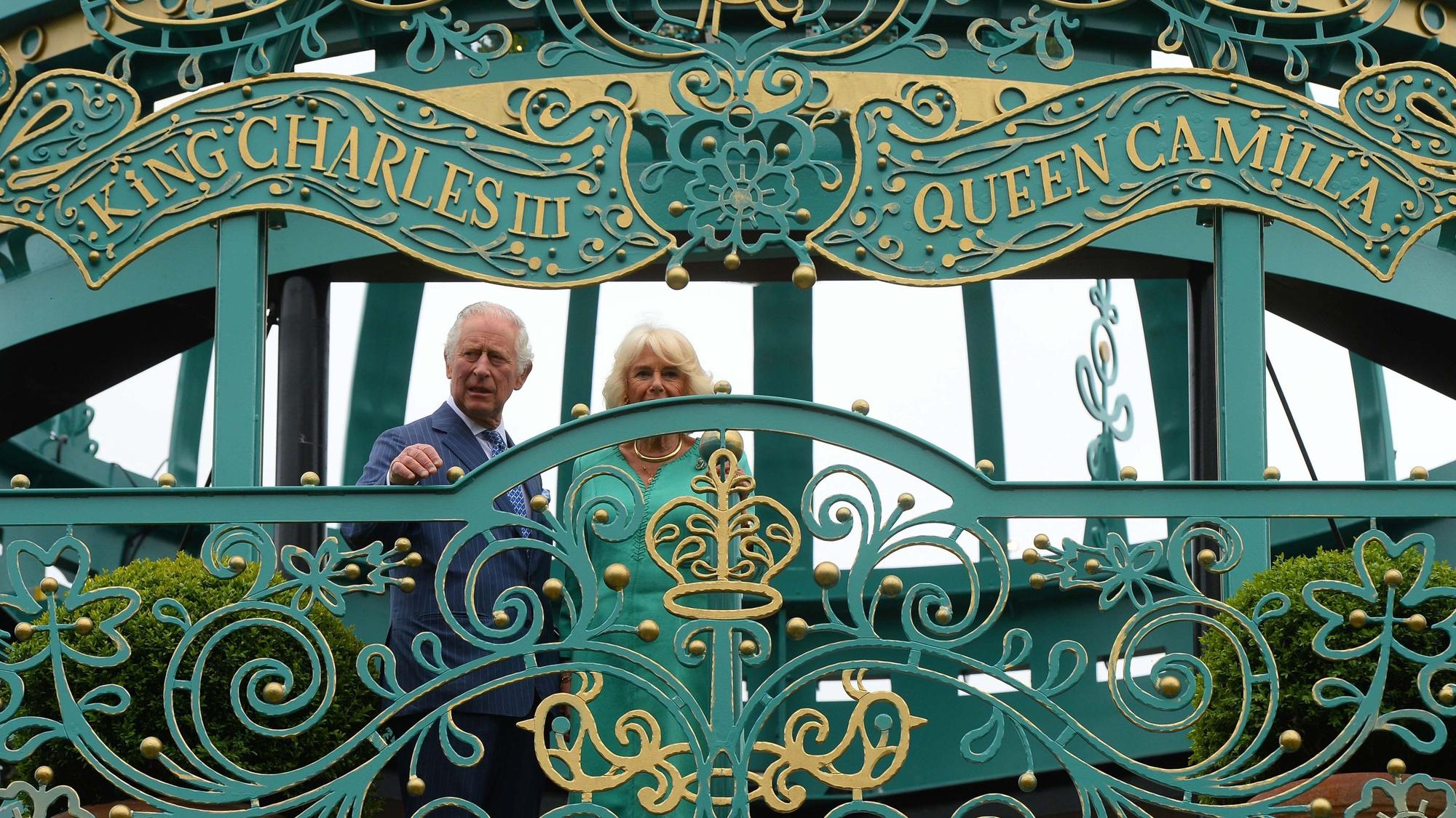 König Charles III. von Großbritannien und Königin Camilla eröffnen einen neuen Krönungsgarten. Sie stehen vor dessen Toren. Darüber stehen ihre Namen.