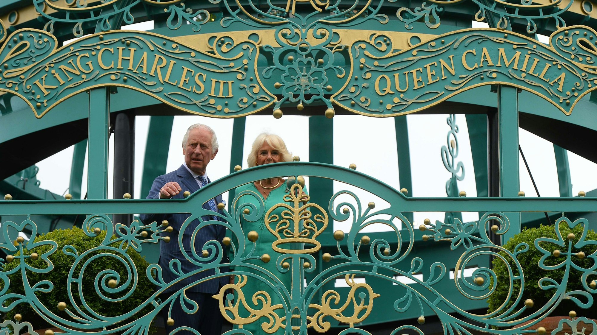 König Charles III. von Großbritannien und Königin Camilla eröffnen einen neuen Krönungsgarten. Sie stehen vor dessen Toren. Darüber stehen ihre Namen.