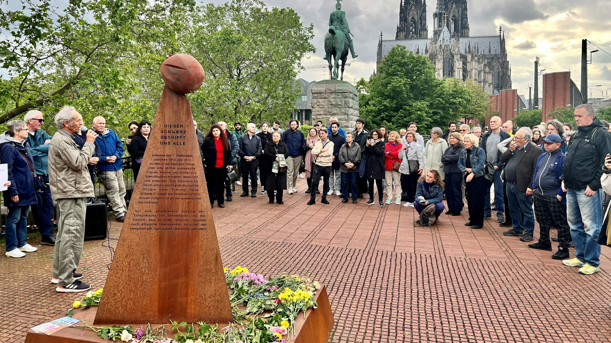 Demonstrierende, die im Kreis vor einem Mahnmal stehen.