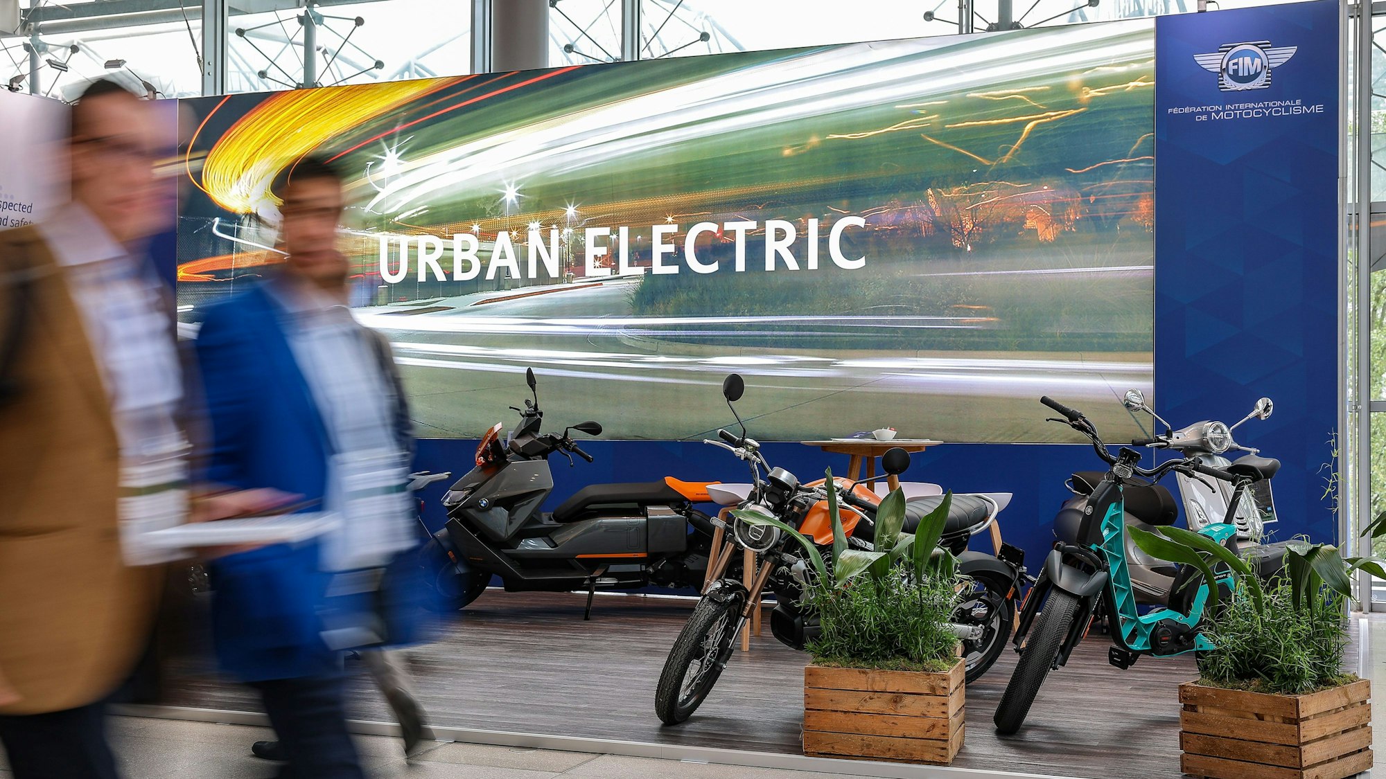 Teilnehmer des Weltgipfels der Verkehrsminister gehen vor einem Stand mit elektrisch angetriebenen Motorrollern und Motorrädern entlang.