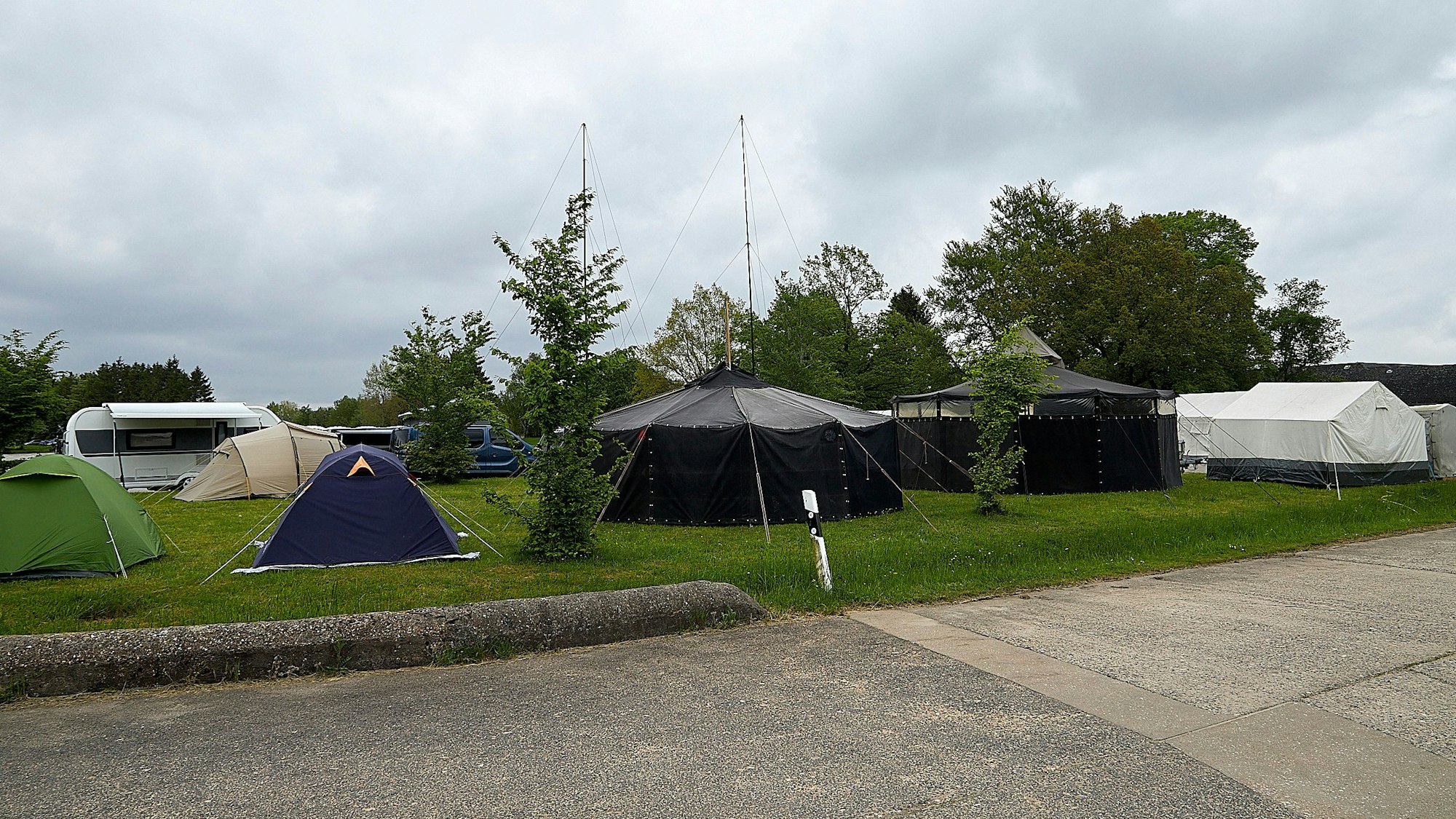 Das Bild zeigt mehrere kleine und drei größere Zelte, die auf einer Wiese aufgebaut sind.