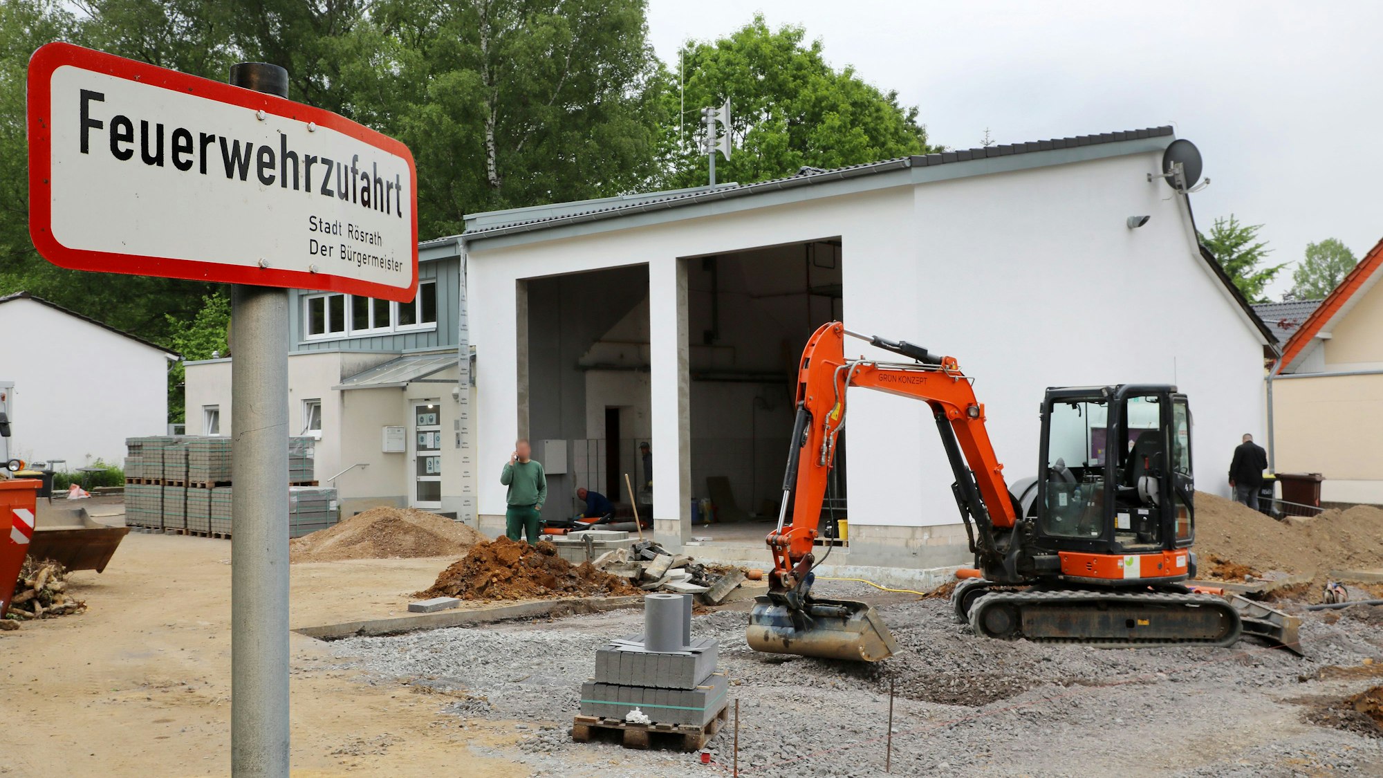 Ein Bagger gräbt vor einer Fahrzeughalle der Feuerwehr.