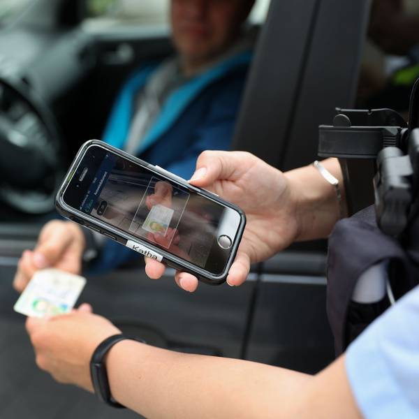 Eine Polizistin hält ein Handy über einen Personalausweis, um Daten zu einer Person abzufragen.