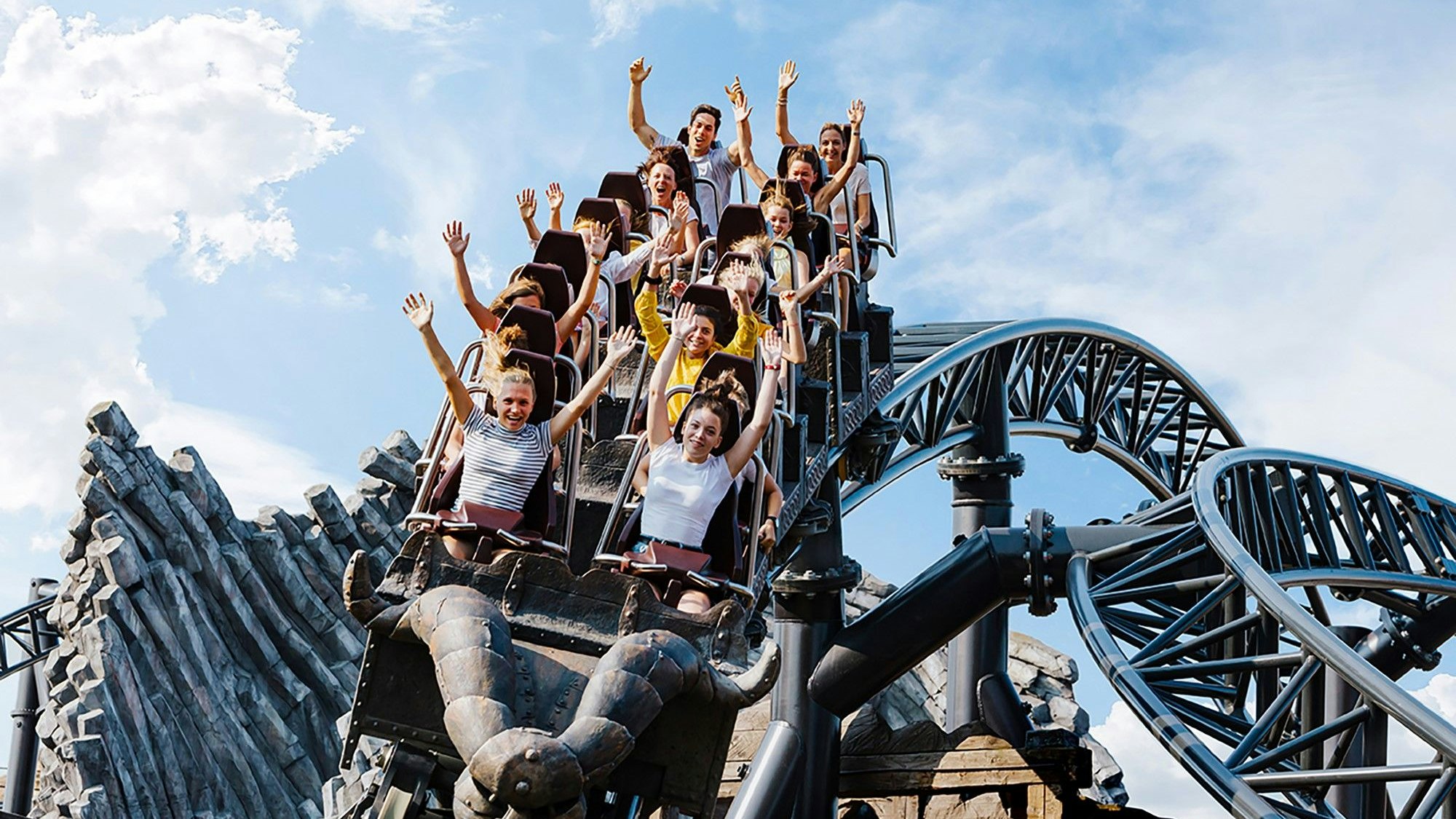 Menschen in einer Achterbahn reißen ihre Arme nach oben.