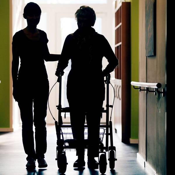 Eine Pflegekraft (l) begleitet die Bewohnerin eines Altenheims beim Gang über den Flur.