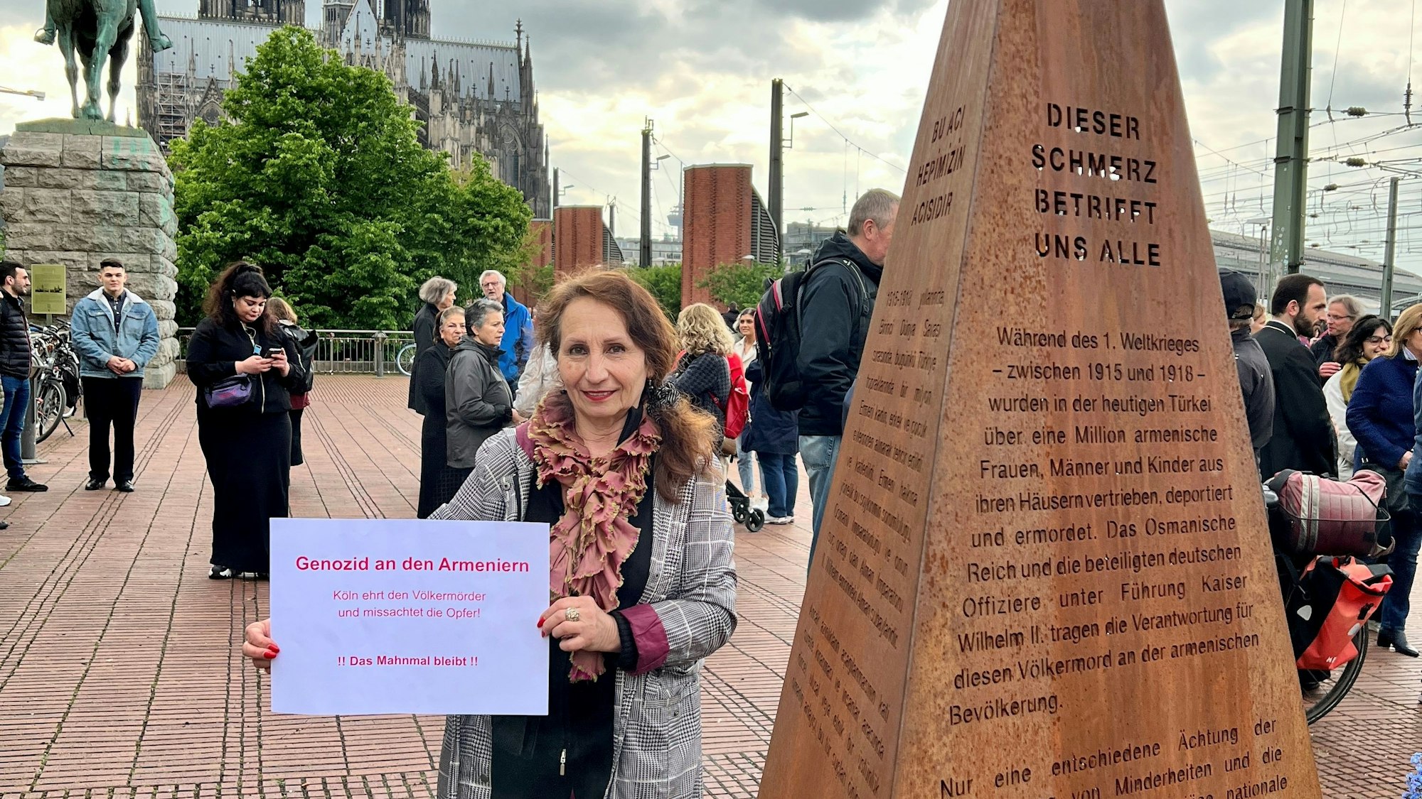 Eine Demonstrantin hält bei einer Kundgebung vor dem Mahnmals für den Völkermord in Armenien an der Hohenzollernbrücke ein Protest-Schild in die Kamera.