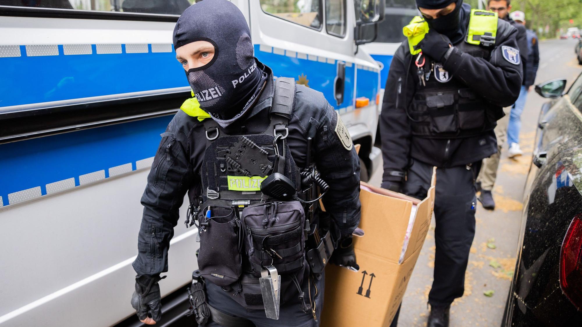 Polizisten tragen bei einer Hausdurchsuchung einen Karton zu einem Fahrzeug. (Symbolbild)