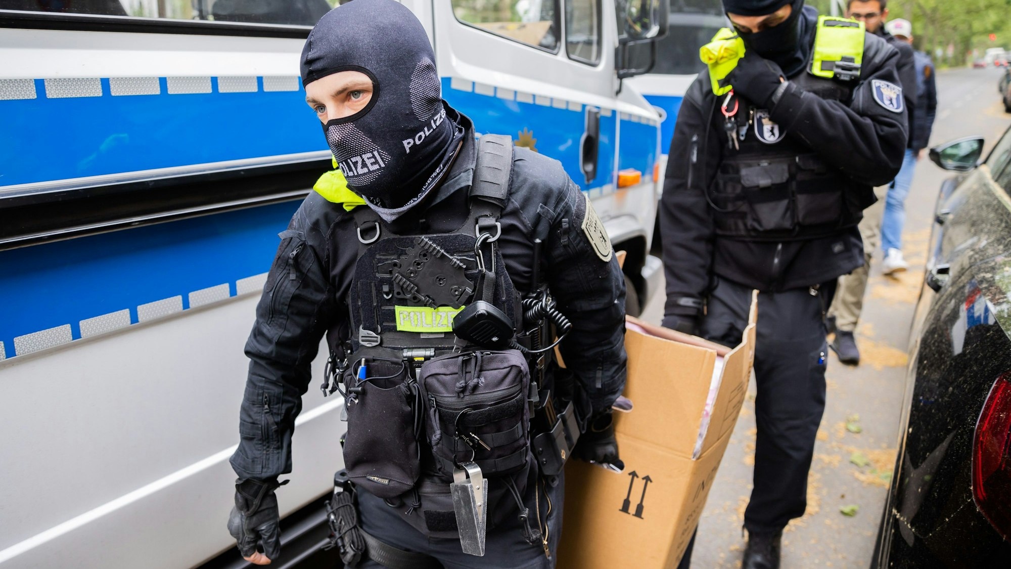Polizisten tragen bei einer Hausdurchsuchung einen Karton zu einem Fahrzeug. (Symbolbild)