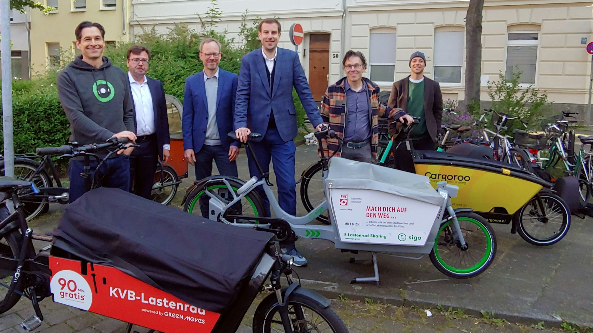 Mehrere Männer, die mit drei verschiedenen Lastenrädern in die Kamera lächeln