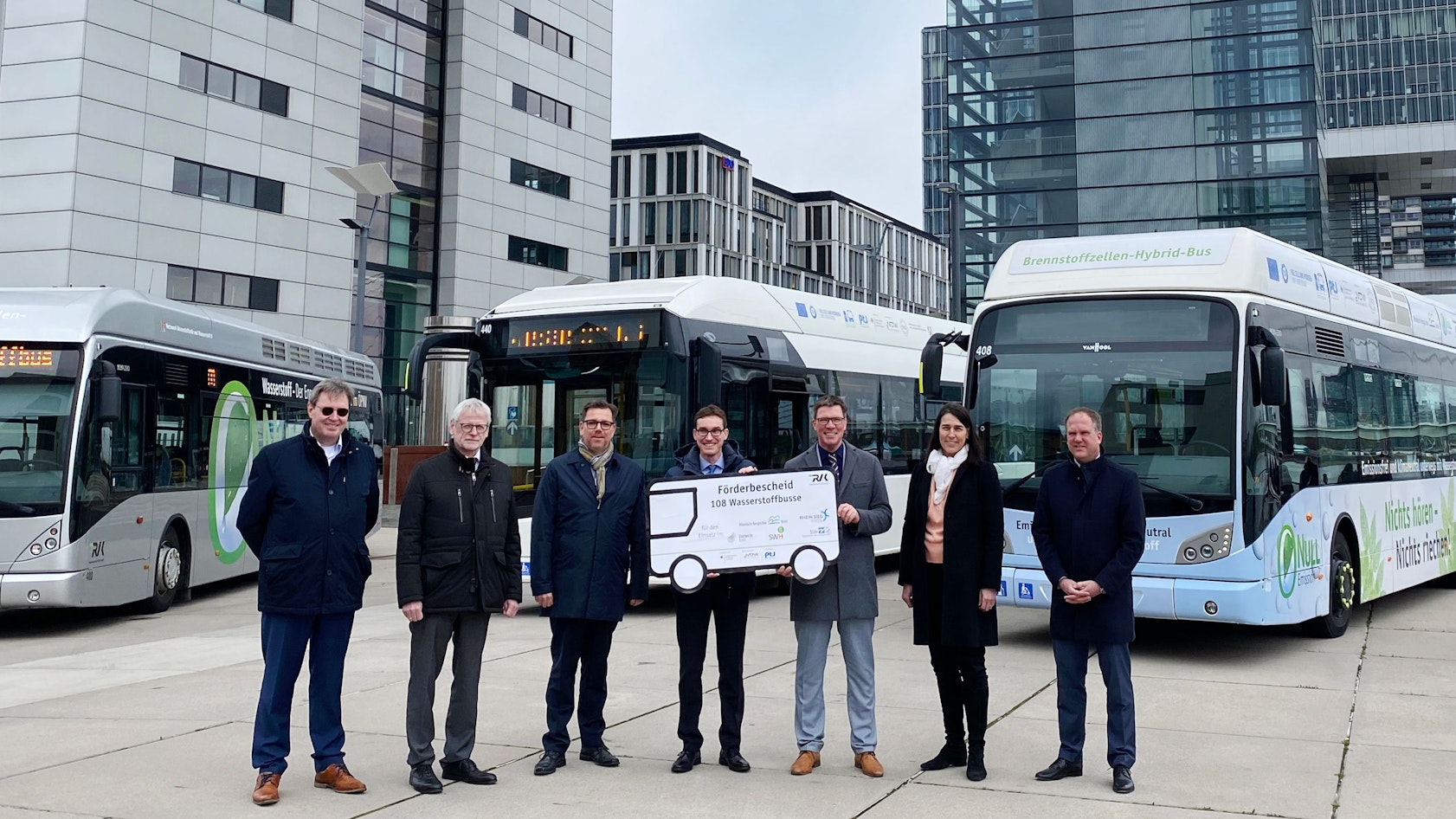 Es sind sieben Personen zu sehen. Zwei von ihnen halten einen großen Förderbescheid.