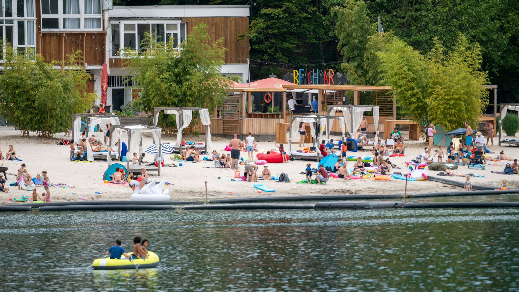 Blick vom Wasser auf einen Sandstrand mit Besuchern auf Handtüchern und Liegen