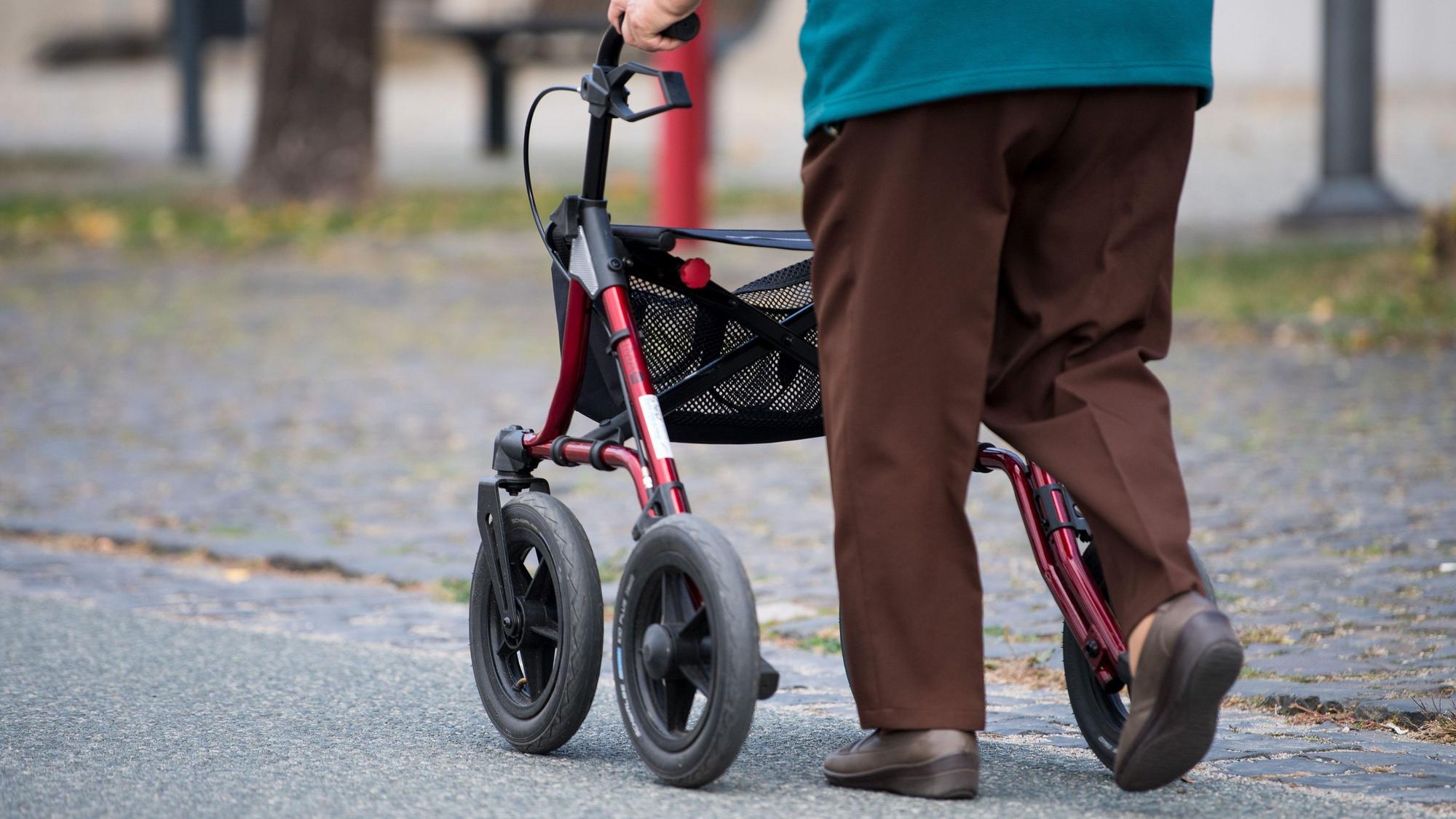 Eine alte Frau geht mit ihrem Rollator über eine Straße.