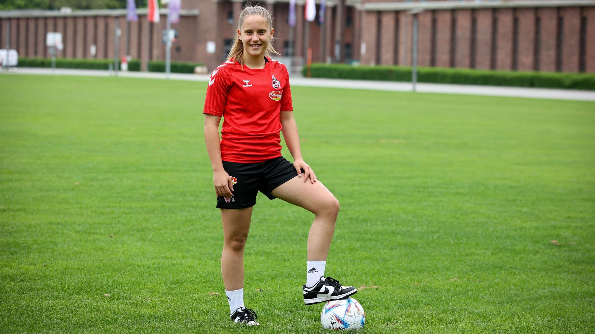Die Kölner Nachwuchs-Fußballerin Lilith Schmidt steht im Trikot des 1.FC Köln mit Ball am Fuß vor dem Rhein-Energie-Stadion.