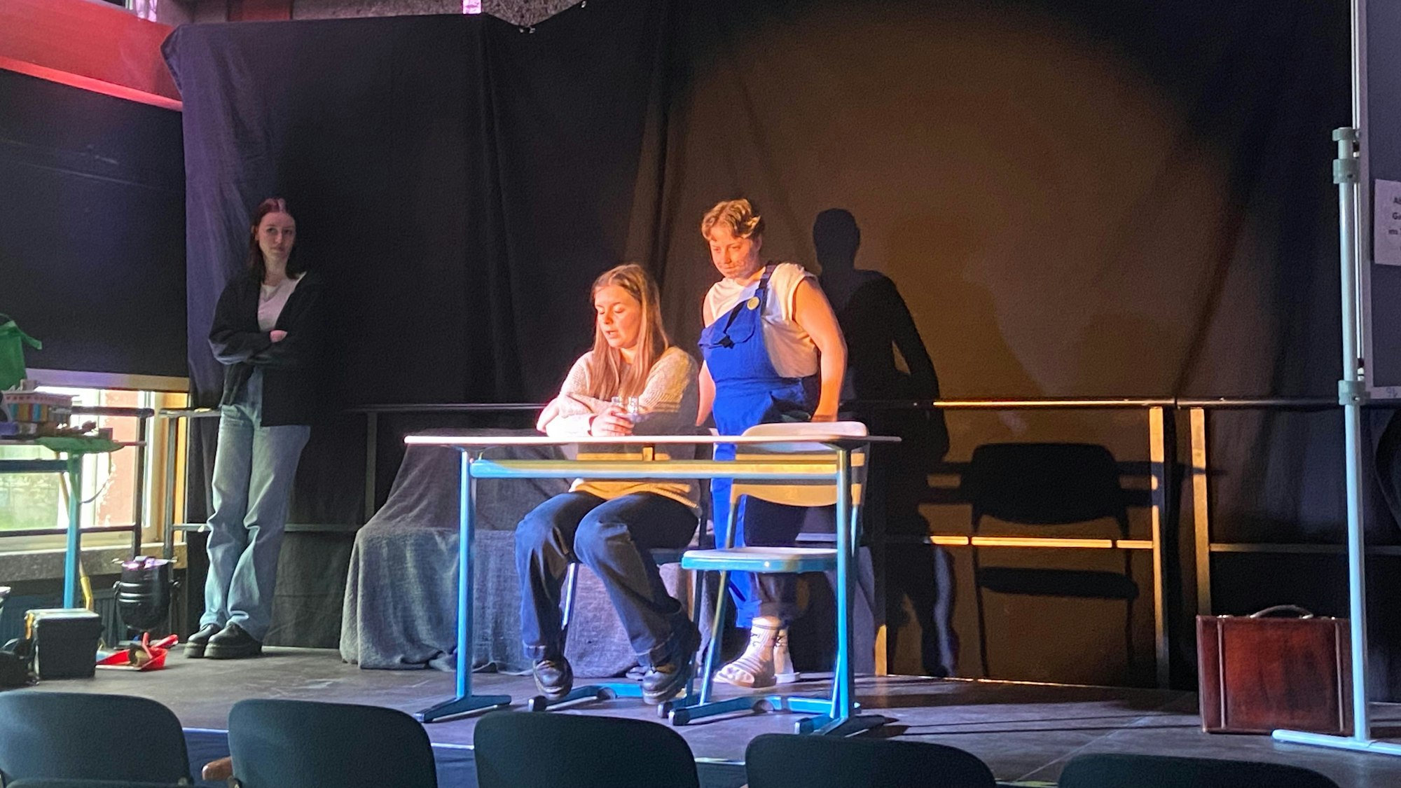 Zwei Schauspielerinnen sitzen auf der Bühne an einem Tisch.