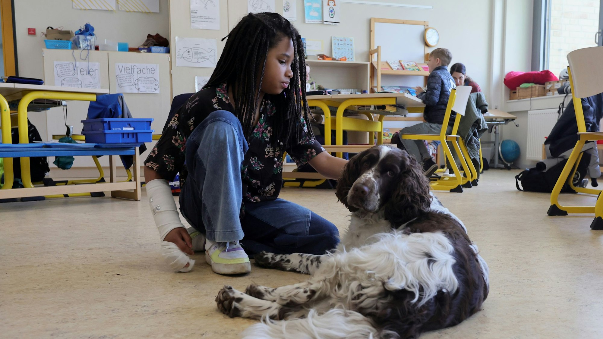 Die Schülerin Fatou sitzt auf dem Boden und krault Hündin Linn.