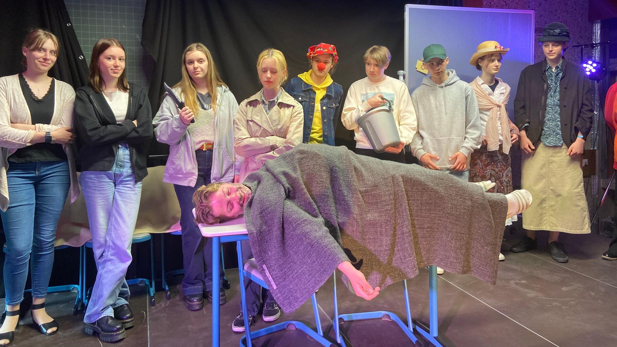 Maja Fleßenkämper liegt auf einem Tisch, die anderen Schülerinnen und Schüler stehen drumherum.