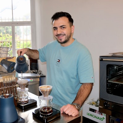 Ein junger Mann füllt heißes Wasser in eine Kaffeekanne mit Filter.