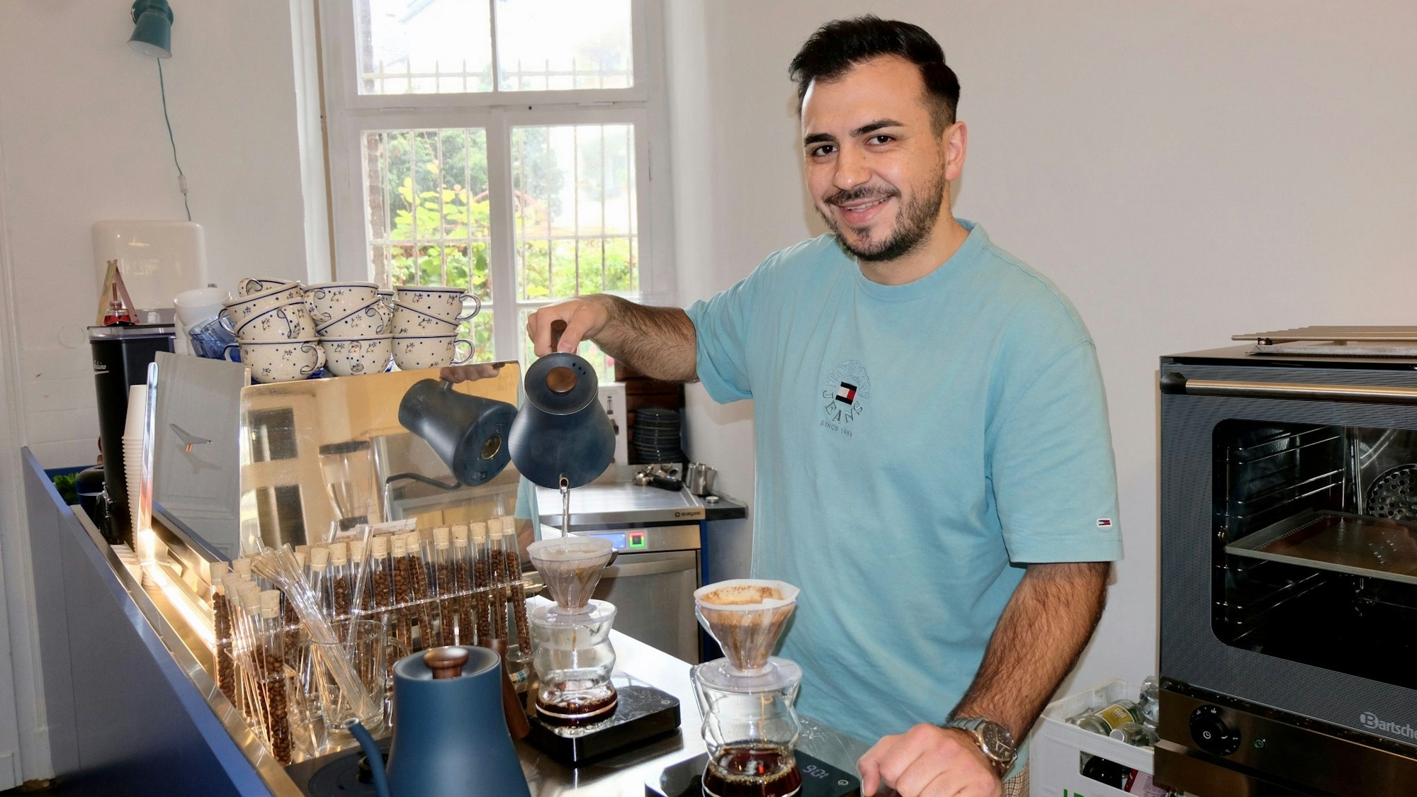 Ein junger Mann füllt heißes Wasser in eine Kaffeekanne mit Filter.