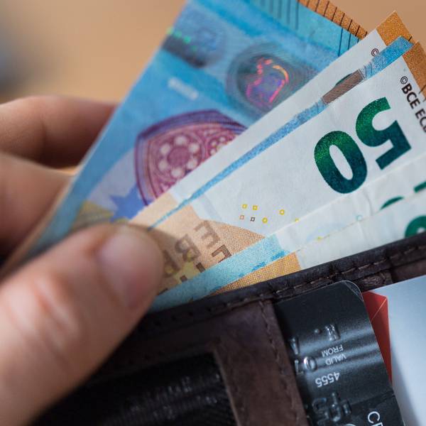 Eine Frau hält eine Geldbörse mit Banknoten und Bankkarten in der Hand.