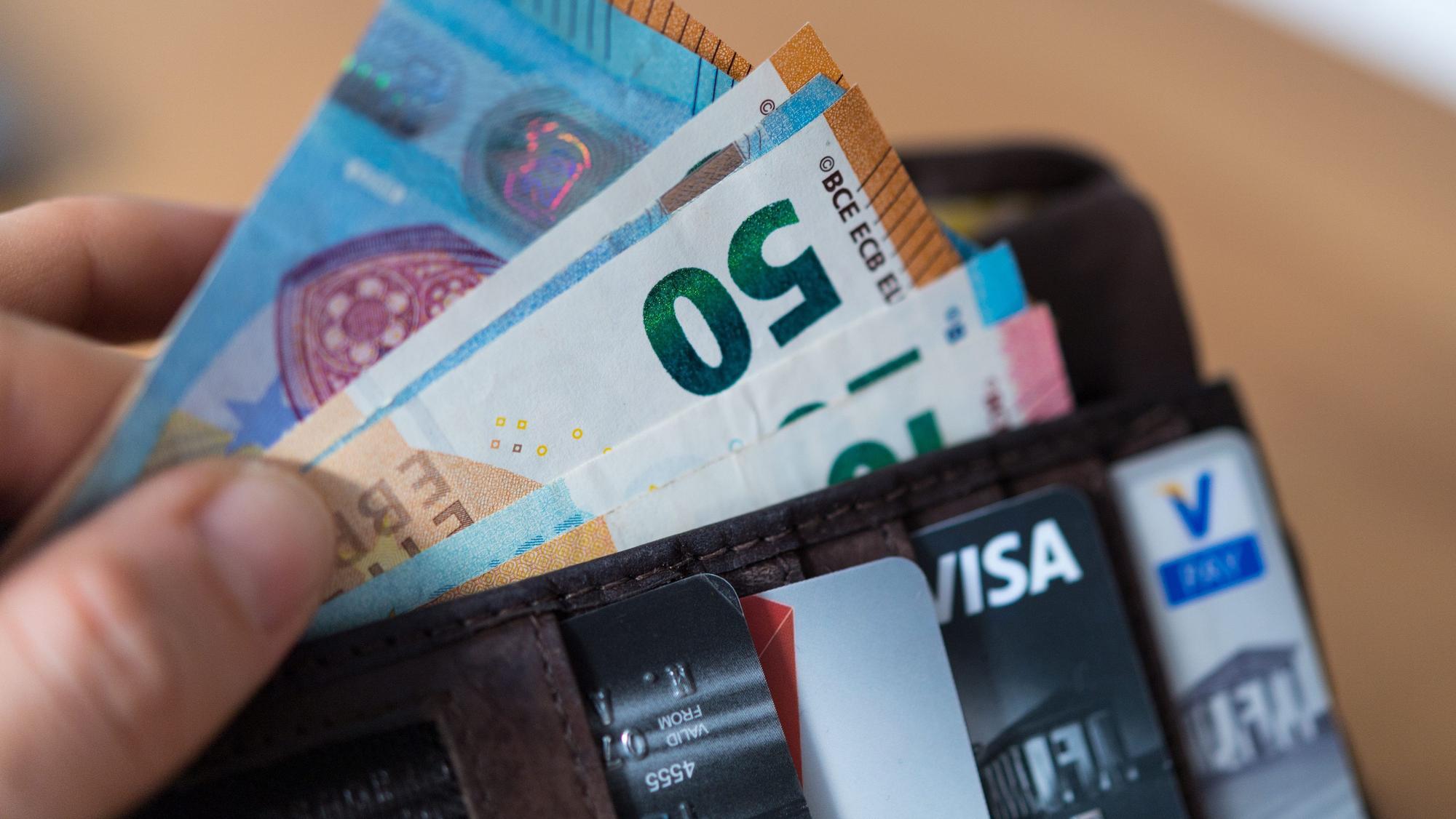 Eine Frau hält eine Geldbörse mit Banknoten und Bankkarten in der Hand.