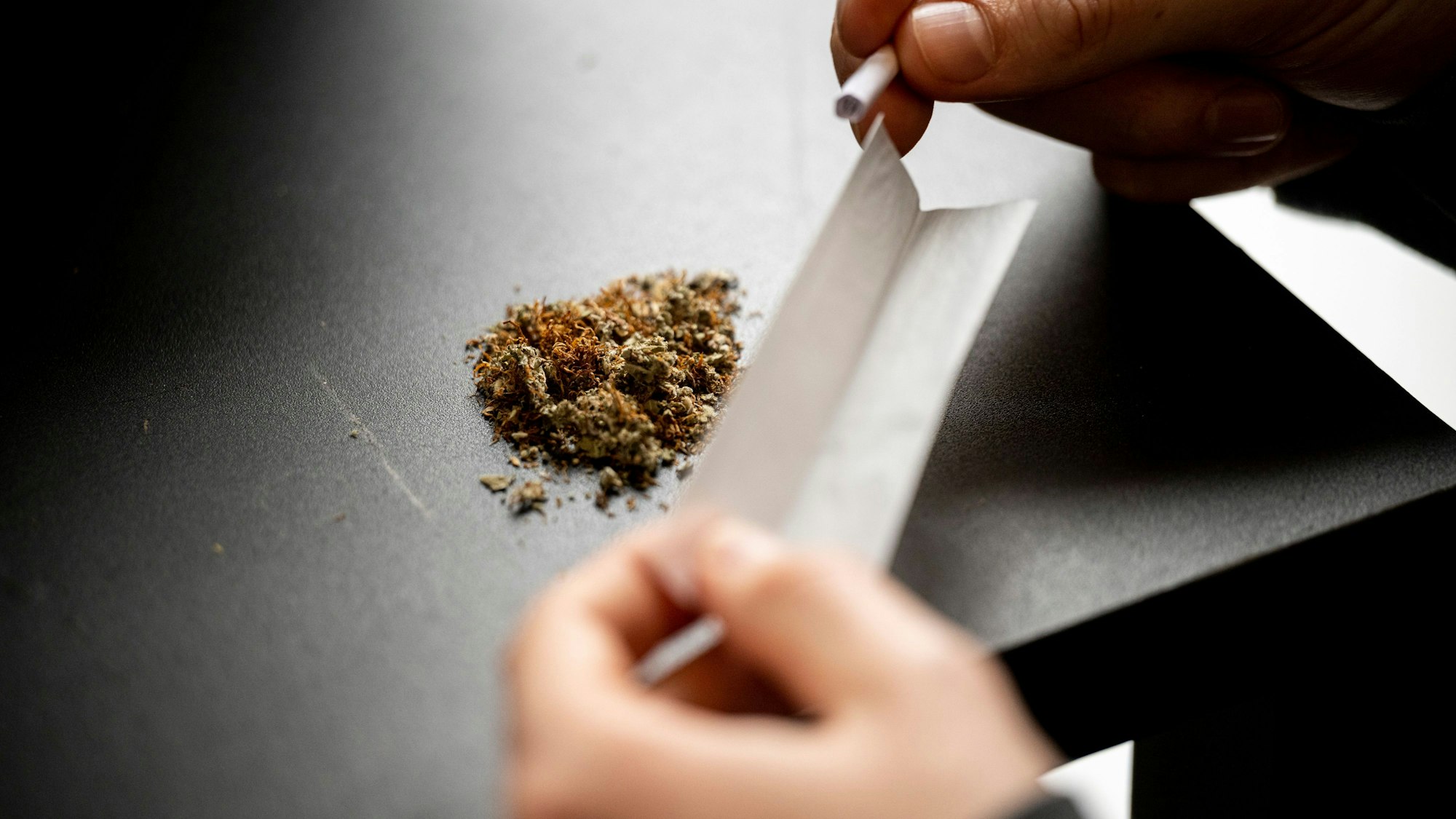 Das Bild zeigt eine Person, die einen Joint dreht.