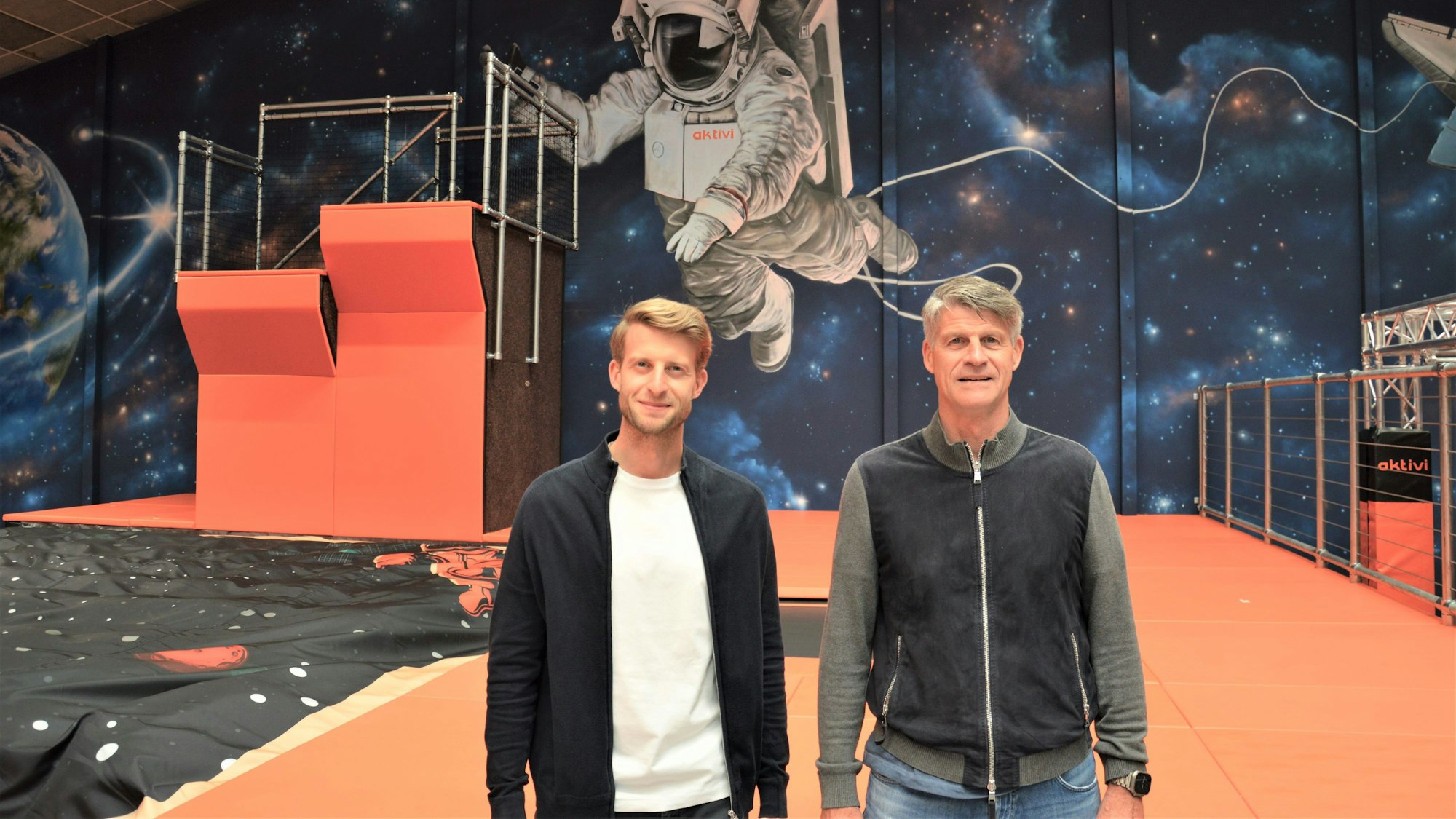 Zwei Männer stehen im Kinderland Aktivi vor einer mit Weltraum-Motiven bemalten Wand.